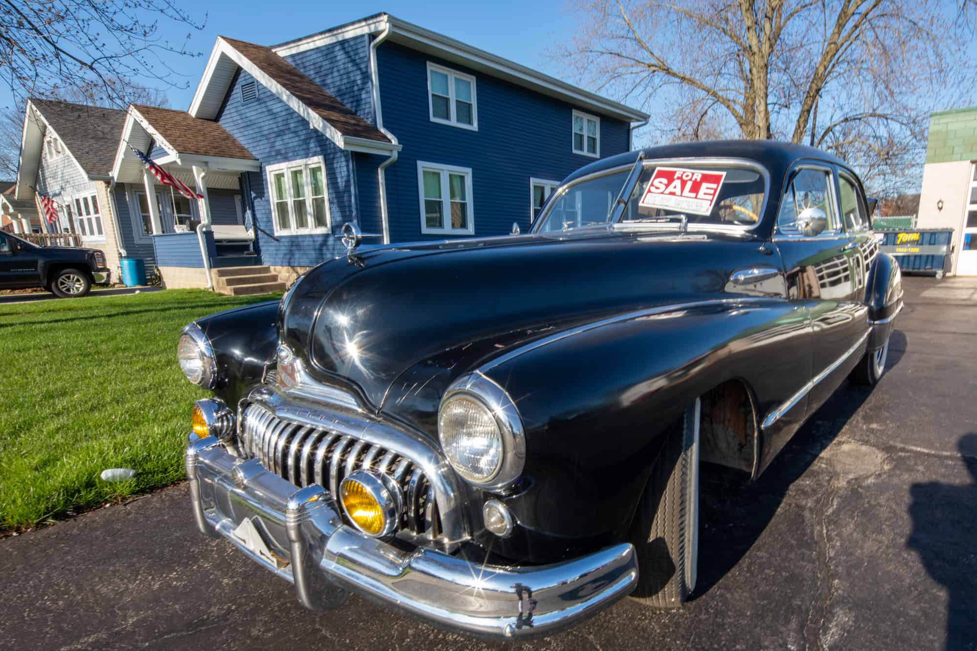 A classic automobile for sale on display at the intersection of Lincoln and 10th. The home behind its modern colors pair with its black finish for an attractive sight as one turns left heading to the lake.